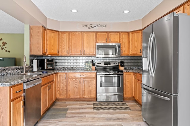 kitchen featuring dark stone countertops, a sink, stainless steel appliances, light wood-style floors, and backsplash