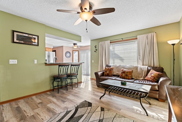 living area featuring a textured ceiling, ceiling fan, light wood-type flooring, and baseboards