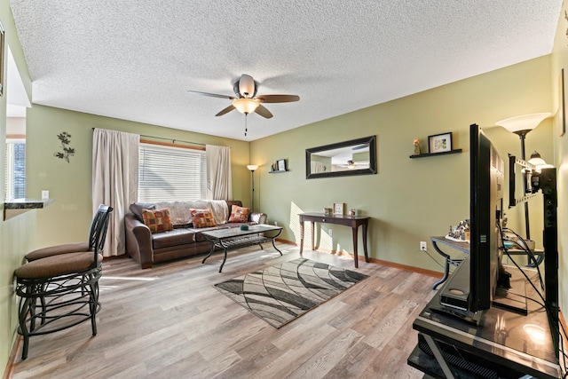 living area featuring a ceiling fan, light wood-type flooring, a textured ceiling, and baseboards