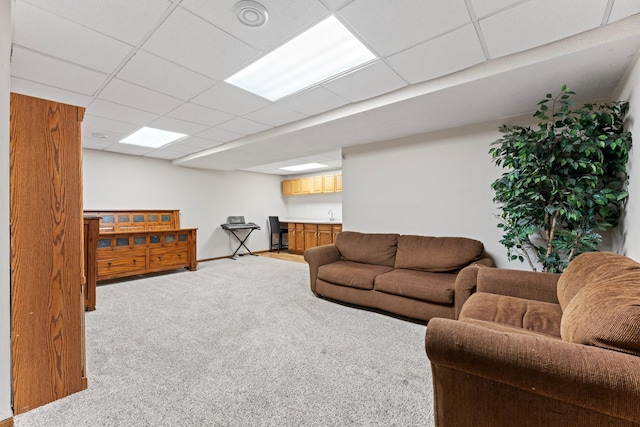 living room with baseboards, a drop ceiling, and light colored carpet