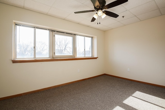 empty room featuring carpet floors, a drop ceiling, a ceiling fan, and baseboards