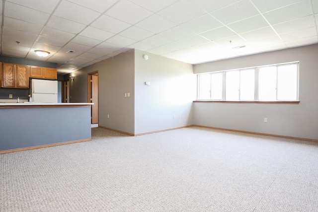 unfurnished living room with a paneled ceiling, light colored carpet, and baseboards