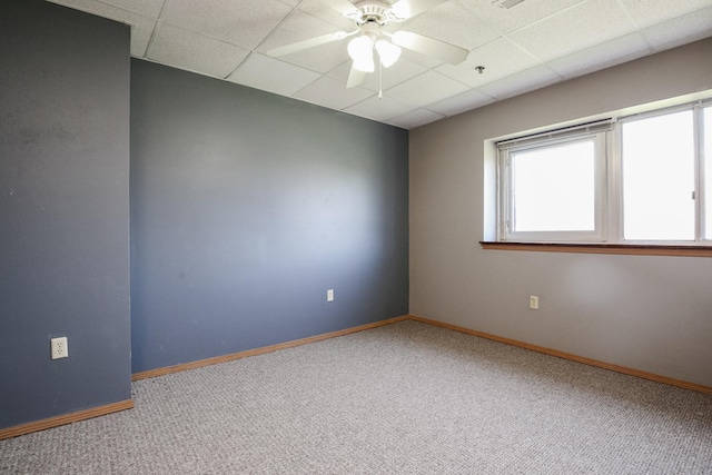 carpeted empty room with a paneled ceiling, ceiling fan, and baseboards