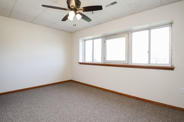 carpeted spare room featuring visible vents, a drop ceiling, and baseboards