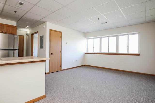 empty room featuring electric panel, visible vents, baseboards, light colored carpet, and a paneled ceiling