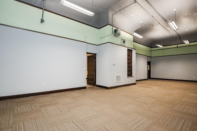 empty room with a towering ceiling, visible vents, light carpet, and baseboards