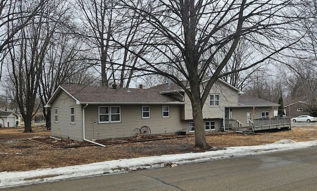 split level home featuring a shingled roof, a chimney, and a wooden deck