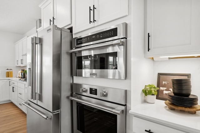 kitchen with stainless steel appliances, light wood-style floors, light countertops, and white cabinets