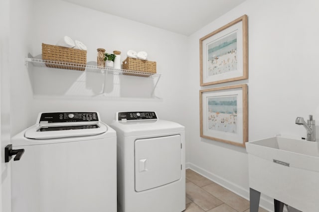 clothes washing area with washer and clothes dryer, light tile patterned floors, a sink, laundry area, and baseboards