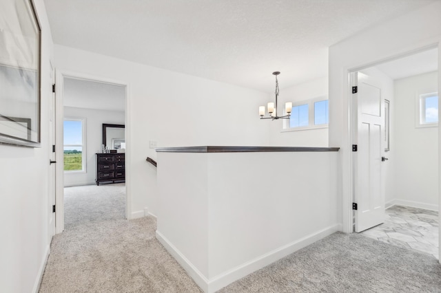 hallway with baseboards, a notable chandelier, an upstairs landing, and light colored carpet