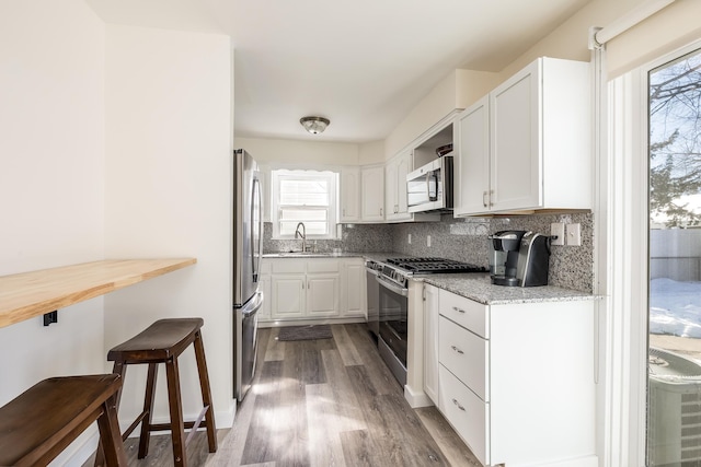 kitchen featuring white cabinets, light stone counters, a sink, stainless steel appliances, and backsplash