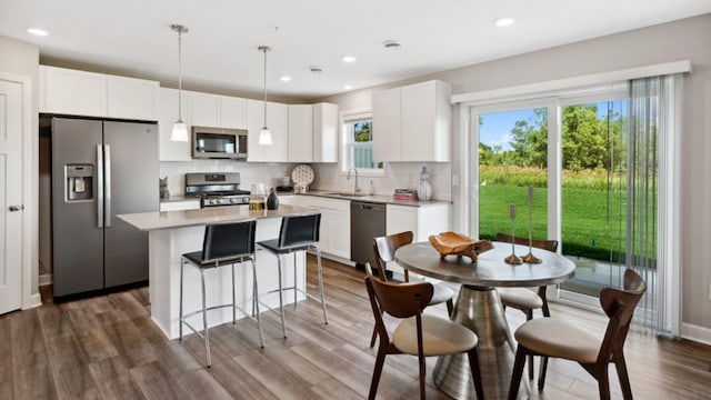 kitchen with a kitchen island, decorative backsplash, white cabinets, stainless steel appliances, and a sink