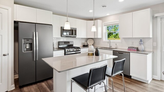 kitchen with wood finished floors, a sink, stainless steel appliances, white cabinets, and tasteful backsplash