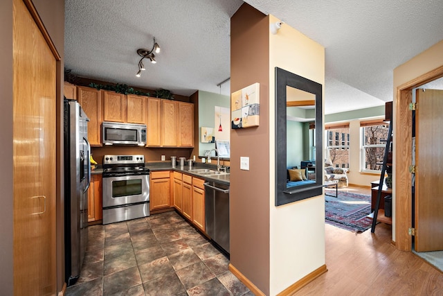 kitchen with dark countertops, appliances with stainless steel finishes, brown cabinetry, a sink, and a textured ceiling