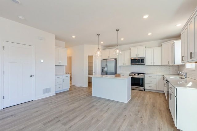 kitchen with appliances with stainless steel finishes, decorative light fixtures, a center island, light countertops, and white cabinetry