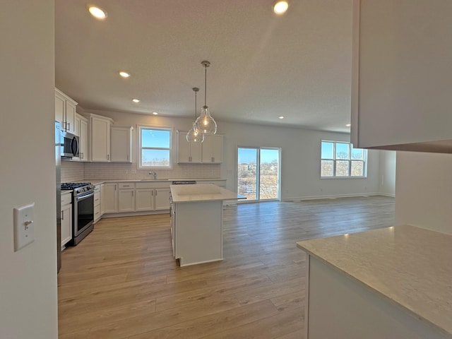 kitchen featuring a kitchen island, appliances with stainless steel finishes, open floor plan, decorative light fixtures, and white cabinetry