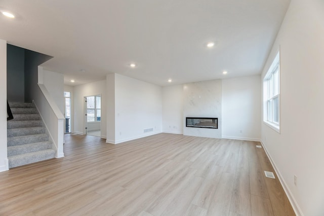 unfurnished living room with light wood-type flooring, a glass covered fireplace, visible vents, and stairway