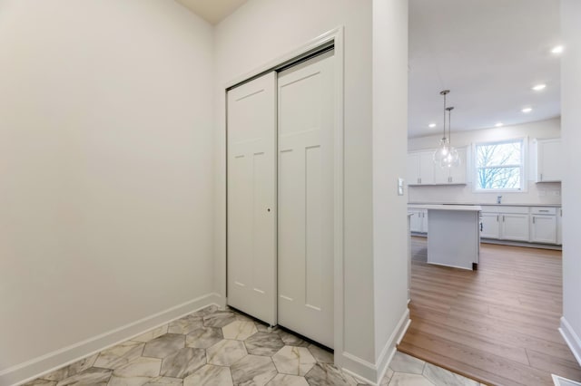 corridor with light wood-style floors, baseboards, a sink, and recessed lighting