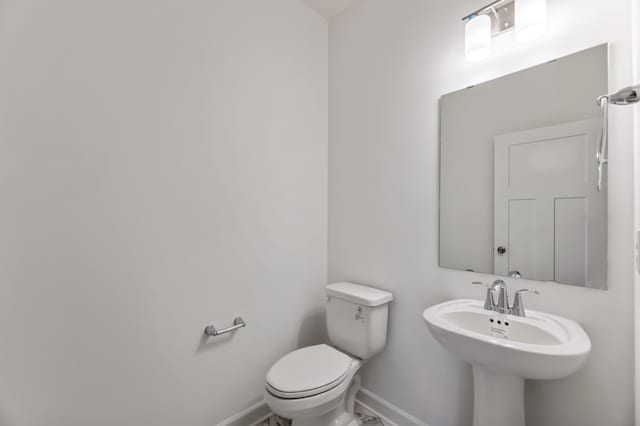 half bath featuring baseboards, a sink, and toilet