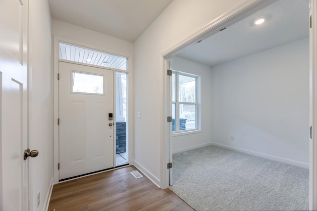 carpeted foyer entrance with visible vents, baseboards, and wood finished floors