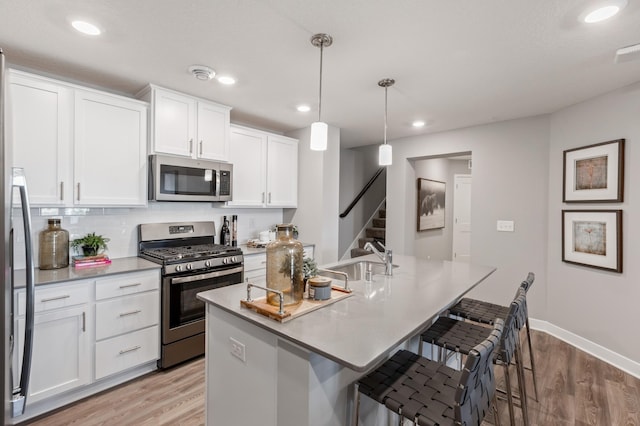 kitchen with a kitchen island with sink, a sink, white cabinetry, appliances with stainless steel finishes, and pendant lighting