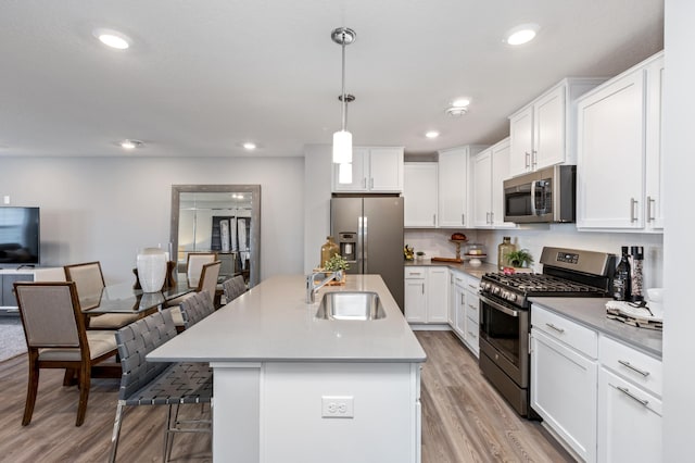 kitchen with appliances with stainless steel finishes, pendant lighting, light countertops, and an island with sink