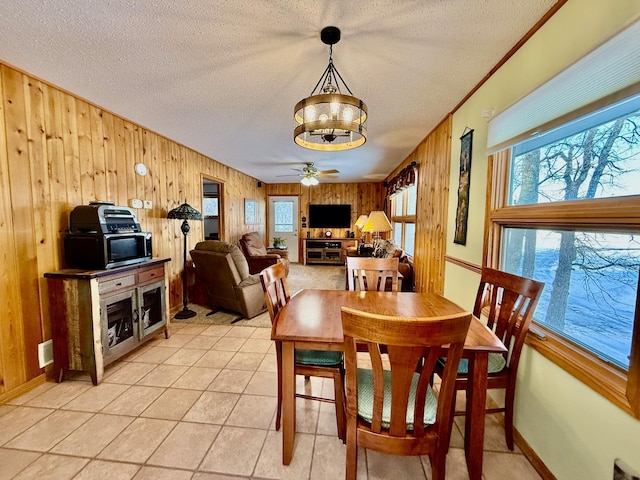 dining space featuring a textured ceiling, ceiling fan, light tile patterned floors, wooden walls, and baseboards