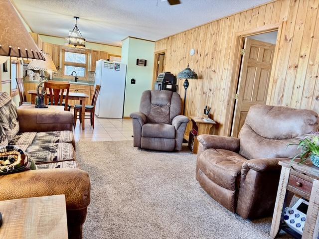 living room featuring light tile patterned floors, ceiling fan, a textured ceiling, wooden walls, and light carpet