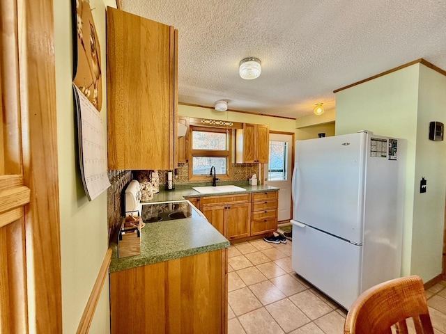 kitchen with brown cabinets, freestanding refrigerator, a sink, backsplash, and light tile patterned flooring