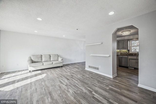 unfurnished living room featuring arched walkways, dark wood-style flooring, visible vents, and baseboards