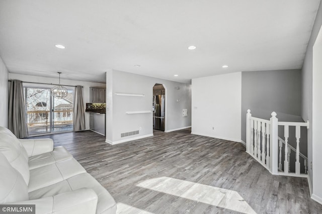 unfurnished living room with arched walkways, visible vents, an inviting chandelier, and wood finished floors