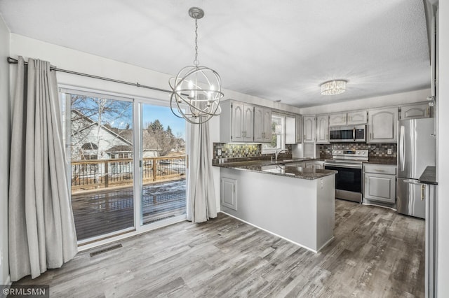 kitchen with decorative backsplash, appliances with stainless steel finishes, a sink, wood finished floors, and a peninsula