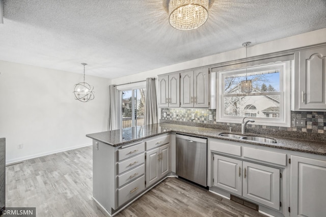 kitchen with dishwasher, light wood-style floors, a sink, and a notable chandelier