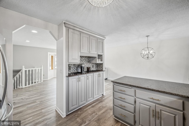 kitchen with gray cabinetry, wood finished floors, hanging light fixtures, dark countertops, and an inviting chandelier