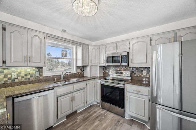 kitchen with stainless steel appliances, dark wood-style flooring, a sink, dark stone counters, and tasteful backsplash