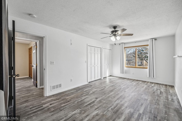 unfurnished bedroom featuring visible vents, dark wood finished floors, baseboards, and two closets