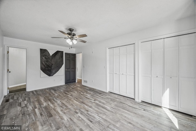 unfurnished bedroom featuring a textured ceiling, a ceiling fan, visible vents, multiple closets, and light wood-type flooring