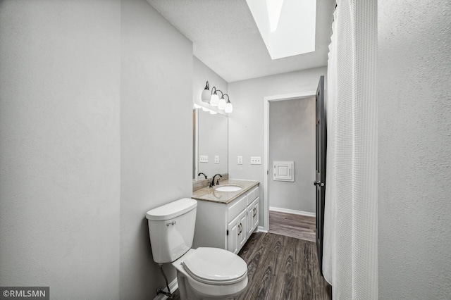 bathroom featuring a skylight, baseboards, toilet, wood finished floors, and vanity