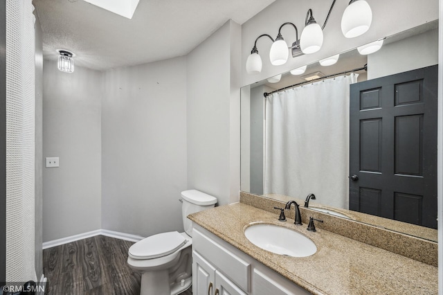 full bath with toilet, a skylight, wood finished floors, vanity, and baseboards