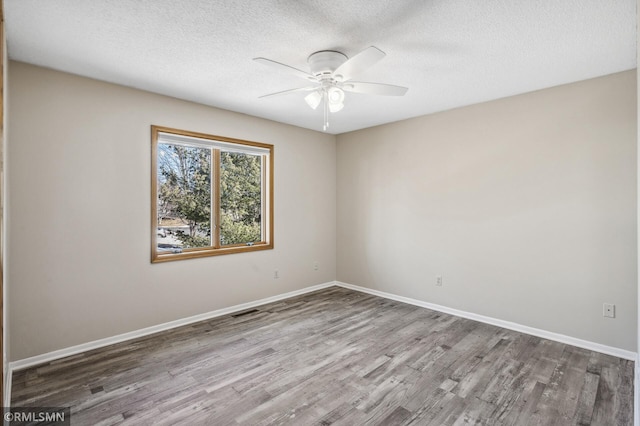 spare room with ceiling fan, a textured ceiling, wood finished floors, visible vents, and baseboards