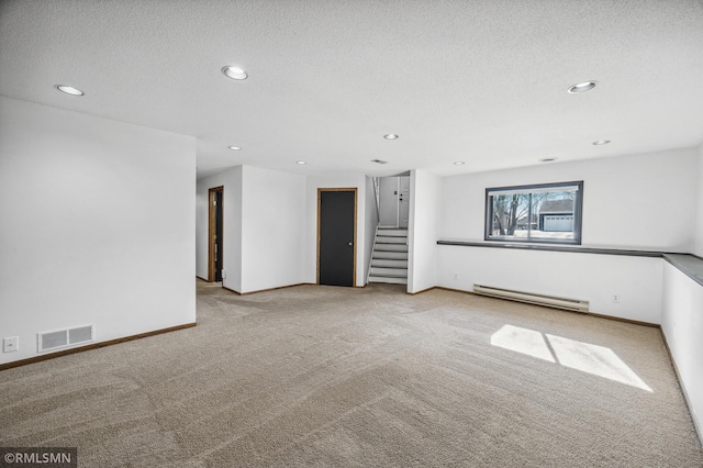 spare room featuring a textured ceiling, a baseboard heating unit, light carpet, visible vents, and stairs