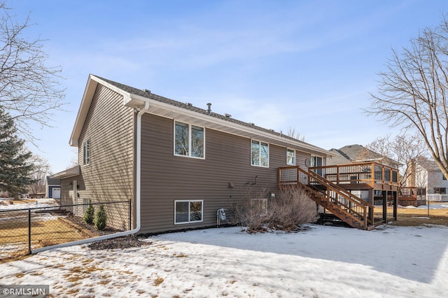 snow covered back of property with fence, a wooden deck, and stairs