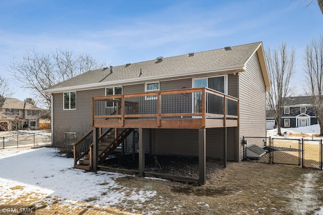 snow covered back of property with roof with shingles, a gate, stairs, fence, and a deck