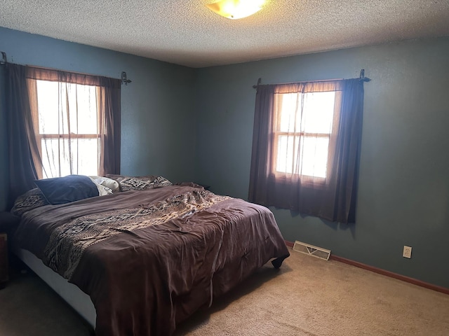 bedroom featuring visible vents, light carpet, a textured ceiling, and multiple windows