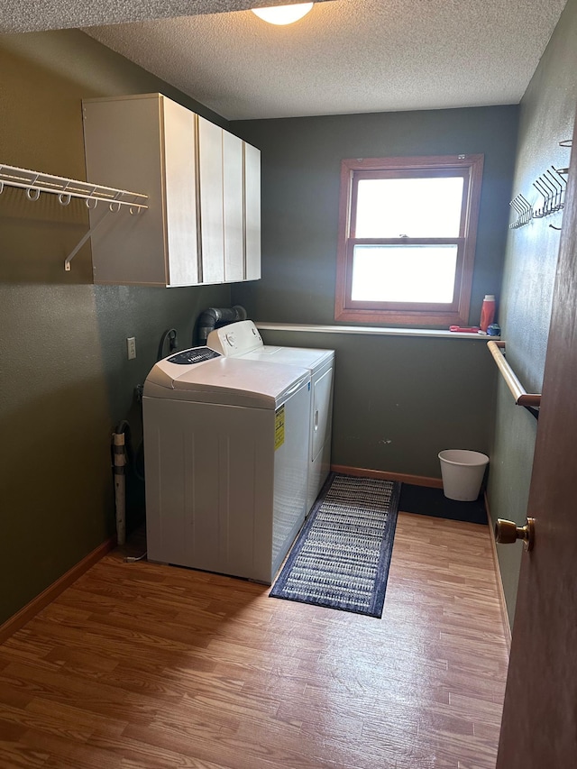 laundry room with cabinet space, washing machine and dryer, light wood-style flooring, and a textured ceiling