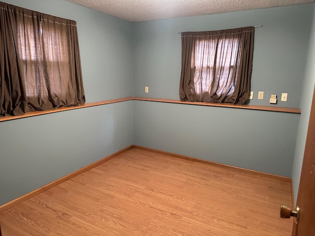 spare room featuring baseboards, light wood-style flooring, and a textured ceiling