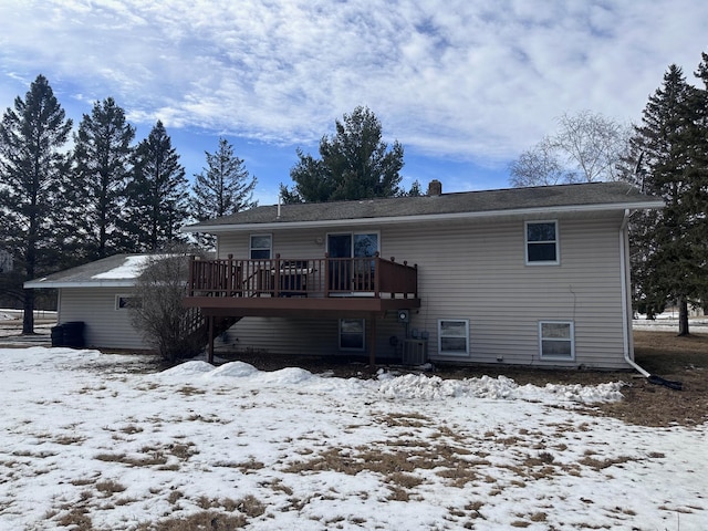 snow covered back of property with a deck, a chimney, and cooling unit