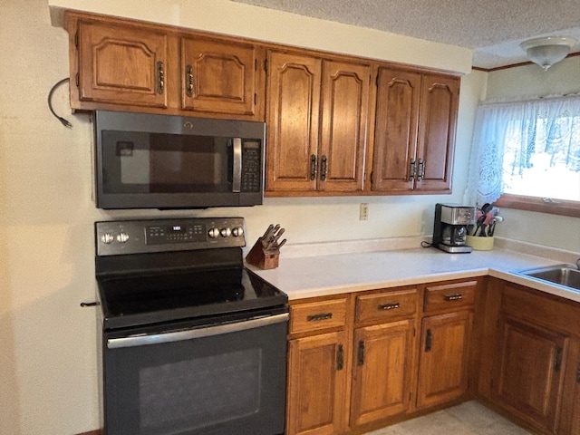 kitchen with brown cabinetry, black / electric stove, light countertops, and a sink