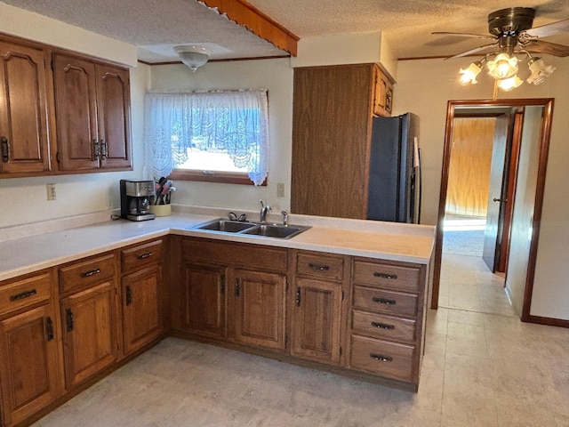 kitchen featuring brown cabinetry, freestanding refrigerator, light countertops, and a sink