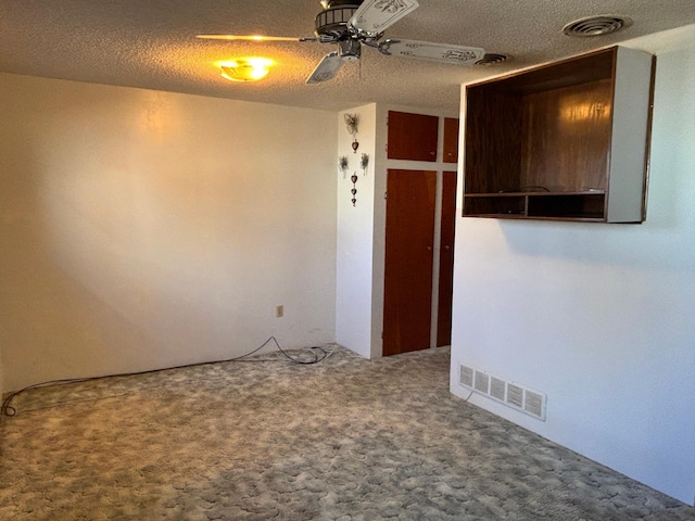 carpeted spare room with a ceiling fan, visible vents, and a textured ceiling